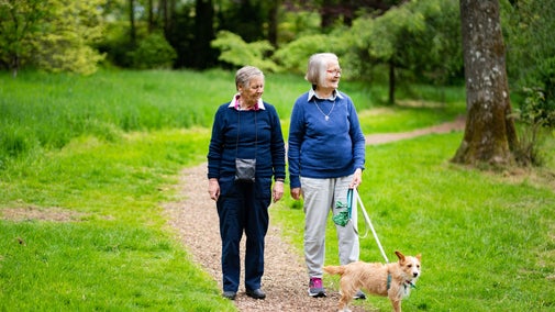 Two older women walk through Rowallane Garden with a dog on a lead